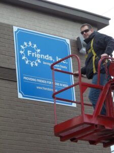 Man installing Friends Inc sign on side of building